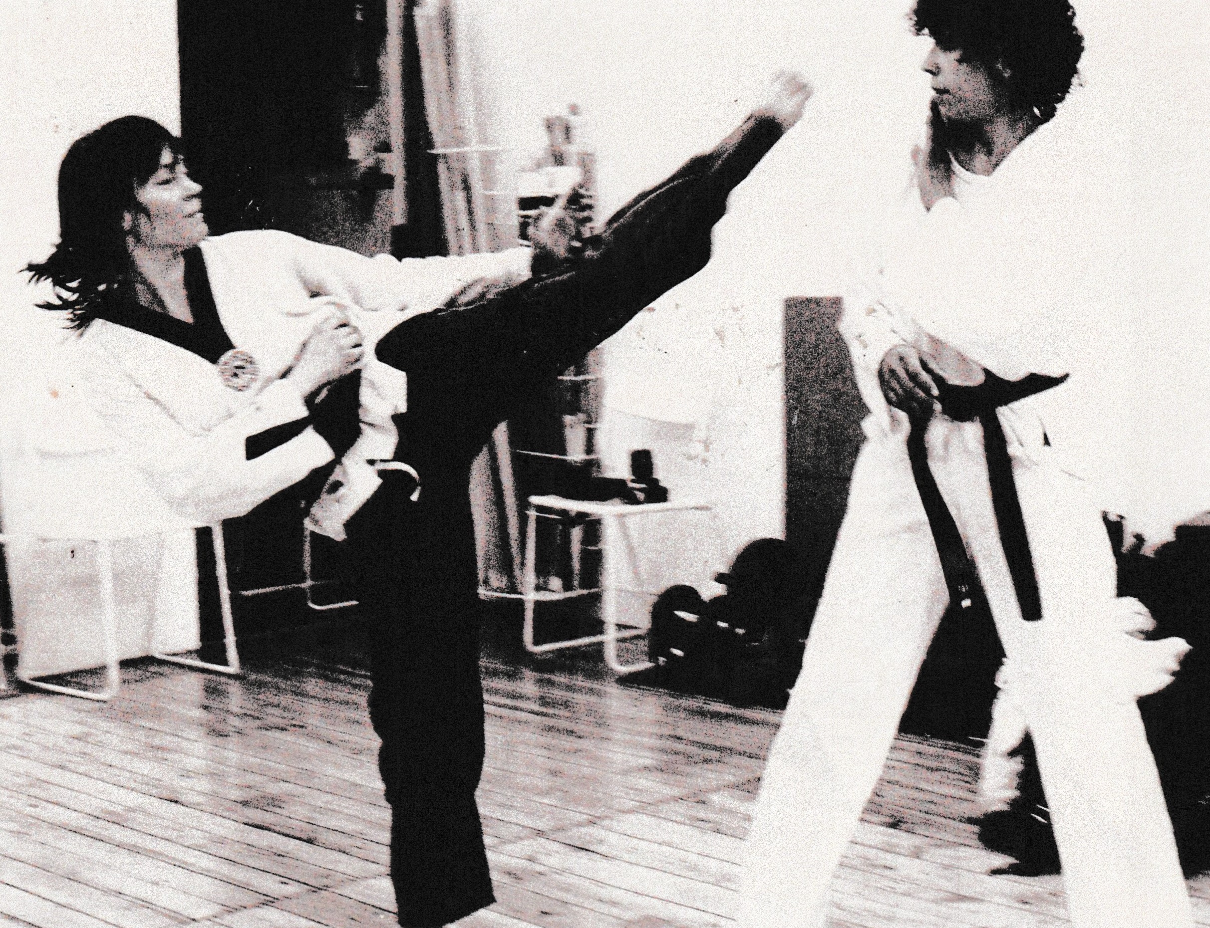 Man sieht auf dieser alten aufnahme Sunny Graff und die Mitgründerin von "Frauen in bewegung". Die beiden Fraueen tragen Taekwondo-Anzüge und trainieren gegen einander. Sunny trittt der anderen Frau dabei auf Kopfhöhe. 