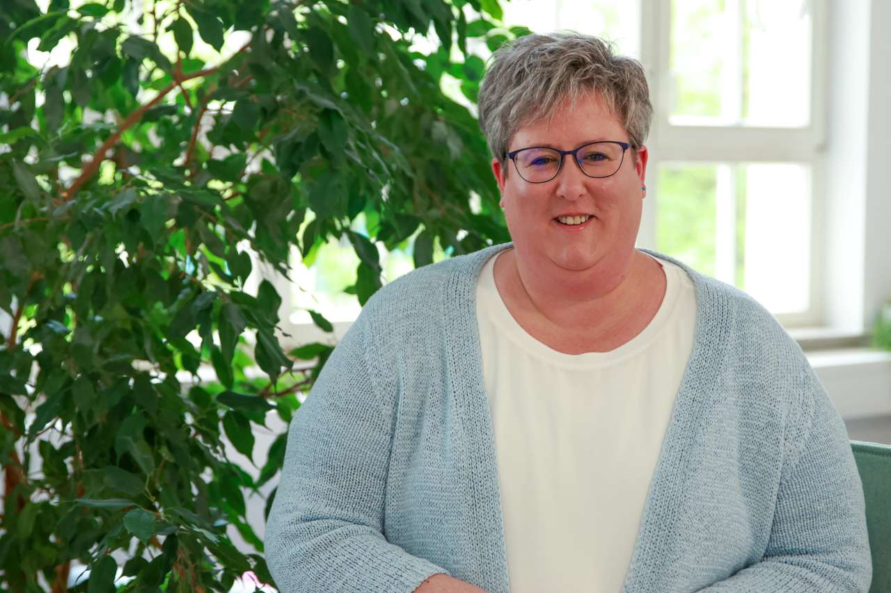 Birgit Rutz steht vor einer Pflanze und lächelt in die Kamera