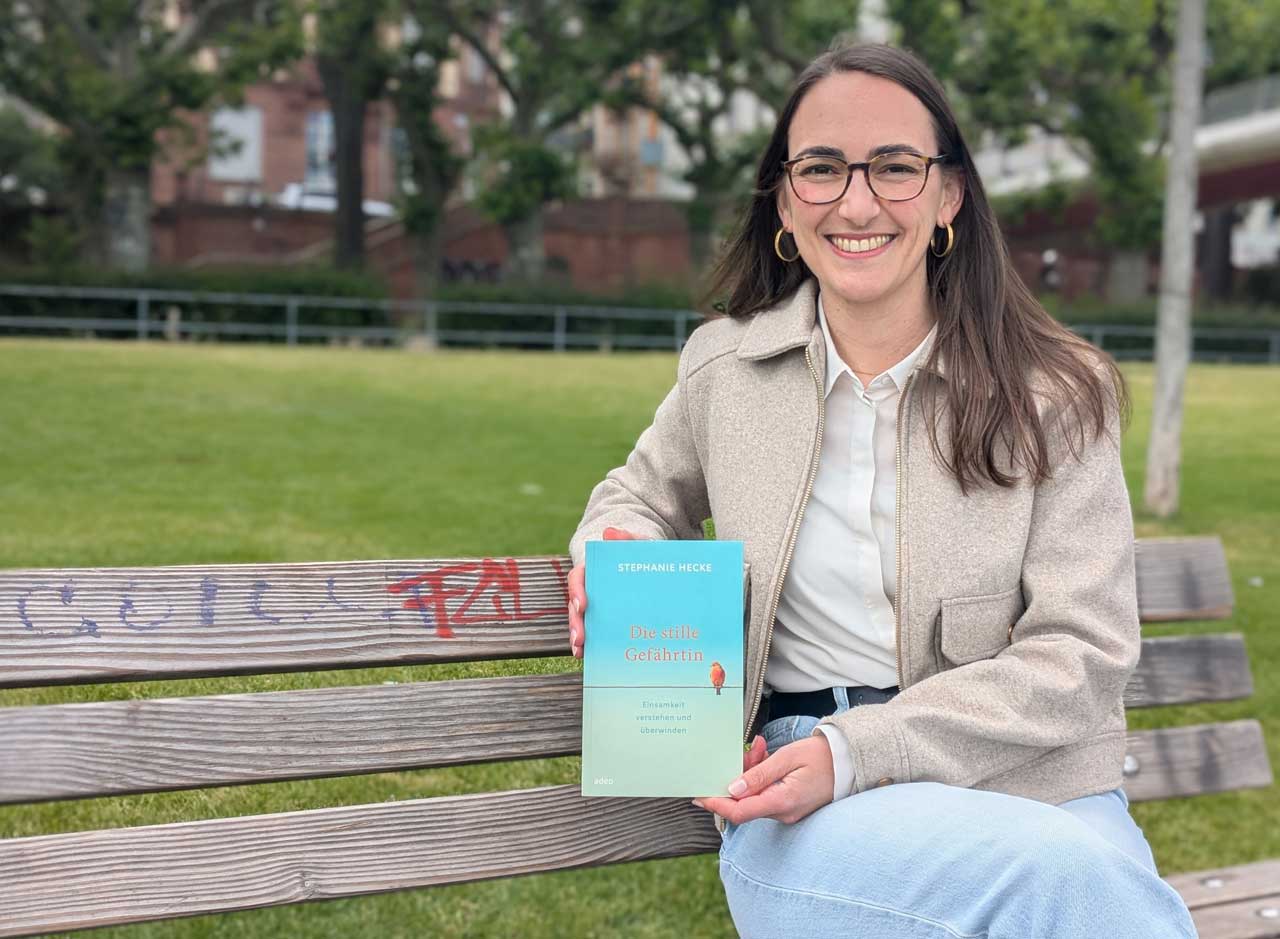 Stephanie Hecke sitzt mit ihrem Buch in den Händen auf einer Bank.