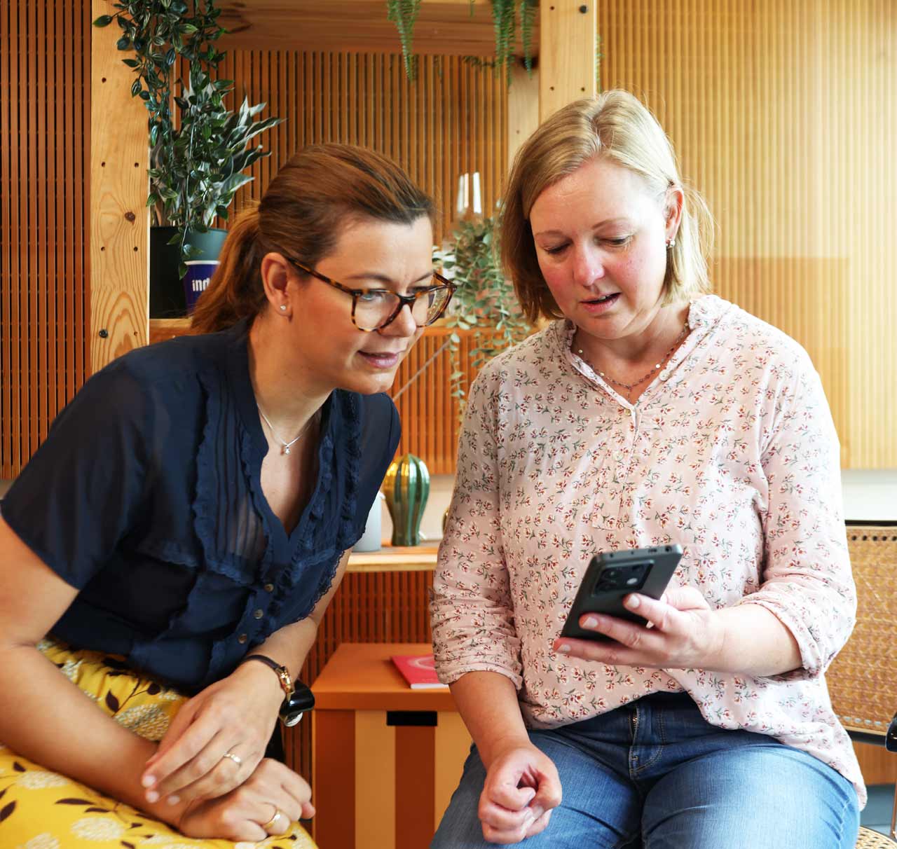 Host Charlotte Mattes schaut auf Smartphone von Stefanie Schuchmann. Sie sitzen im Podcast-Studio in Frankfurt. 