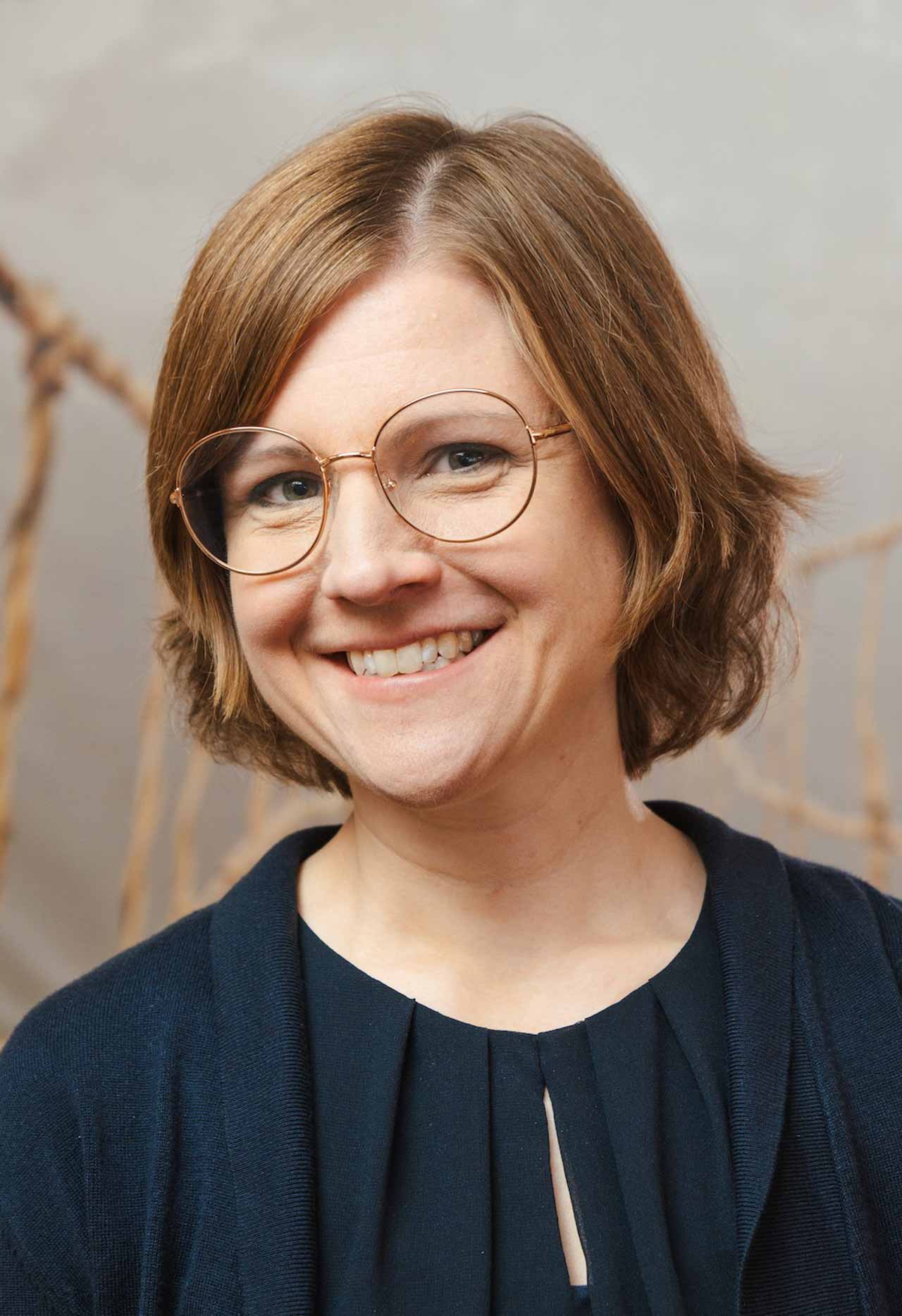 Silke, mit runden Brillengläsern auf der Nase, lächelt in die Kamera. 