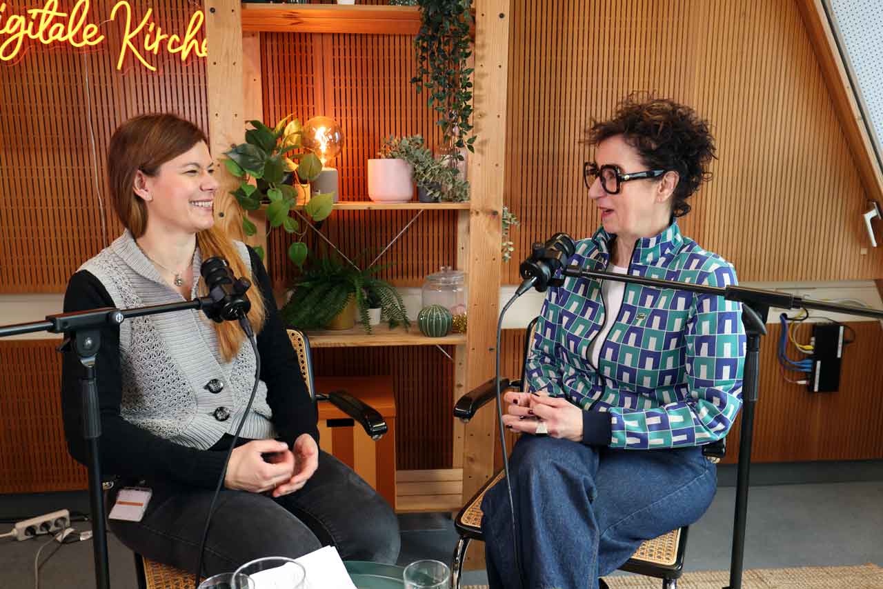 Host Lotte Mattes und Gast Steffi lächeln sich an und sitzen auf Stühlen im Podcast-Studio. 