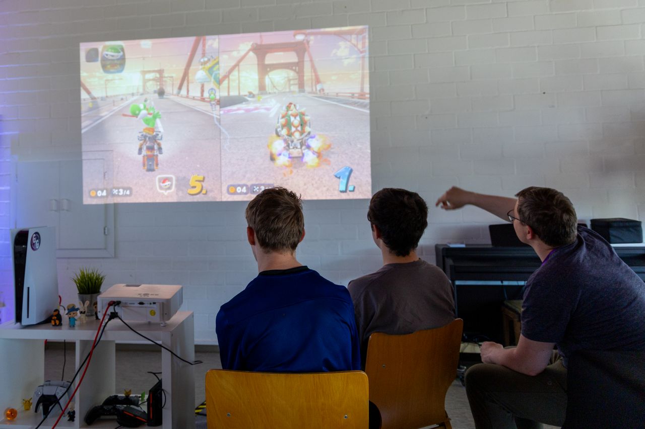 Drei Jugendliche sitzen vor einem Beamer und zocken Mario Kart