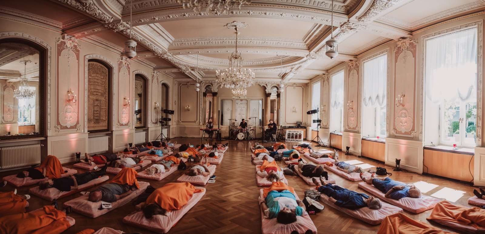 Pompöser Raum mit vielen Menschen auf Matten, die zu Live-Musik schlafen