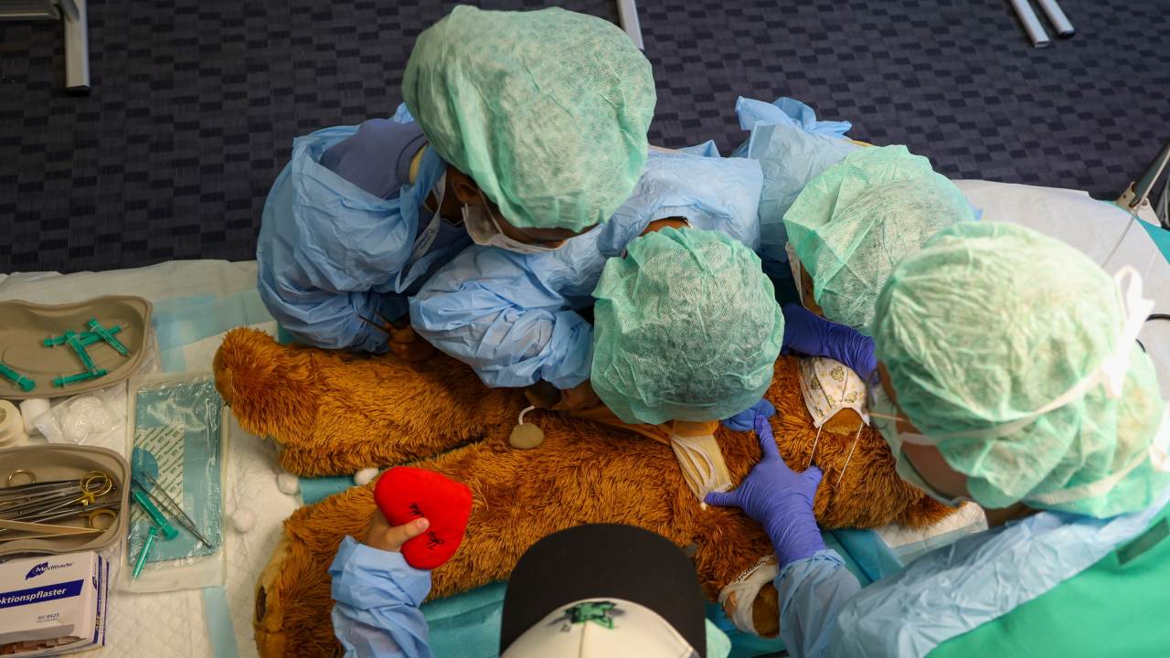 Kinder in OP-Kleidung über einem großen Teddy