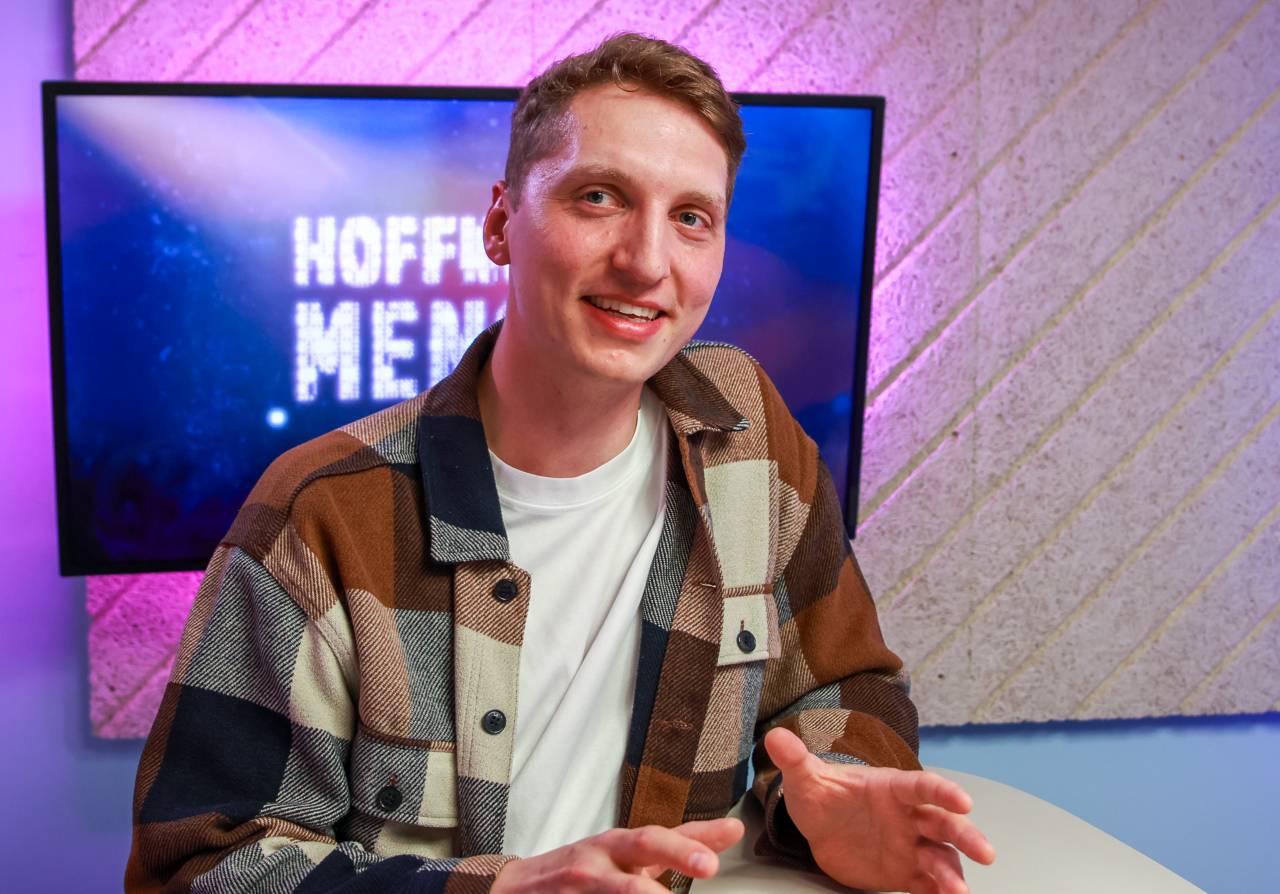Junger Mann mit weißem T-Shirt und offenem Hemd im Podcaststudio