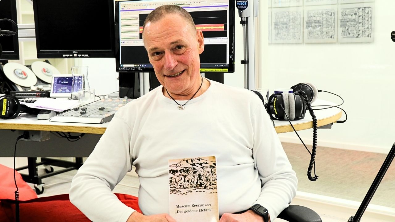 Günther Lietz zeigt stolz sein Buch in die Kamera: Museum Rescue. Er sitzt im Studio des Medienhauses Frankfurt.