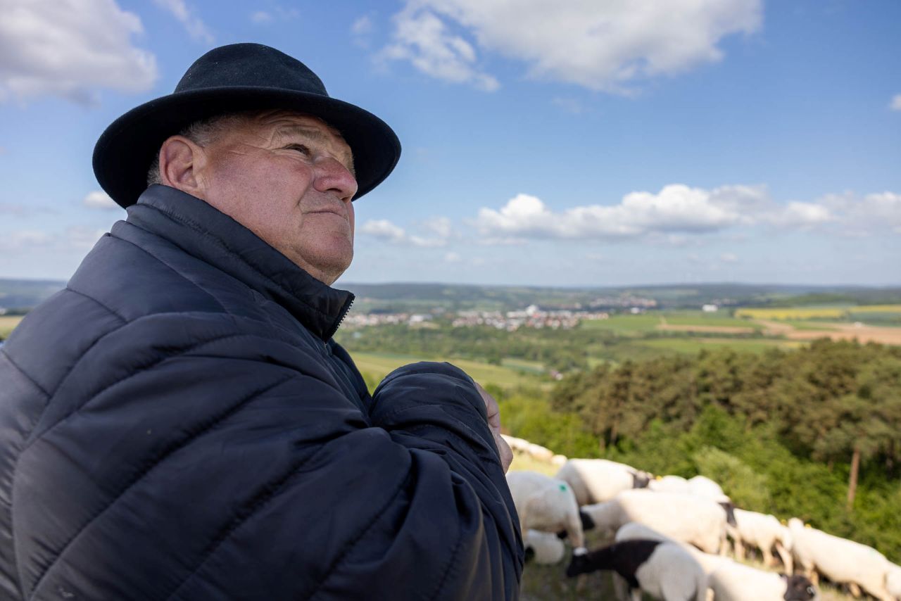 Elmar Spieß mit seinen Schafen in der Rhön, er hat einen Schäferhut auf und blickt in den Himmel
