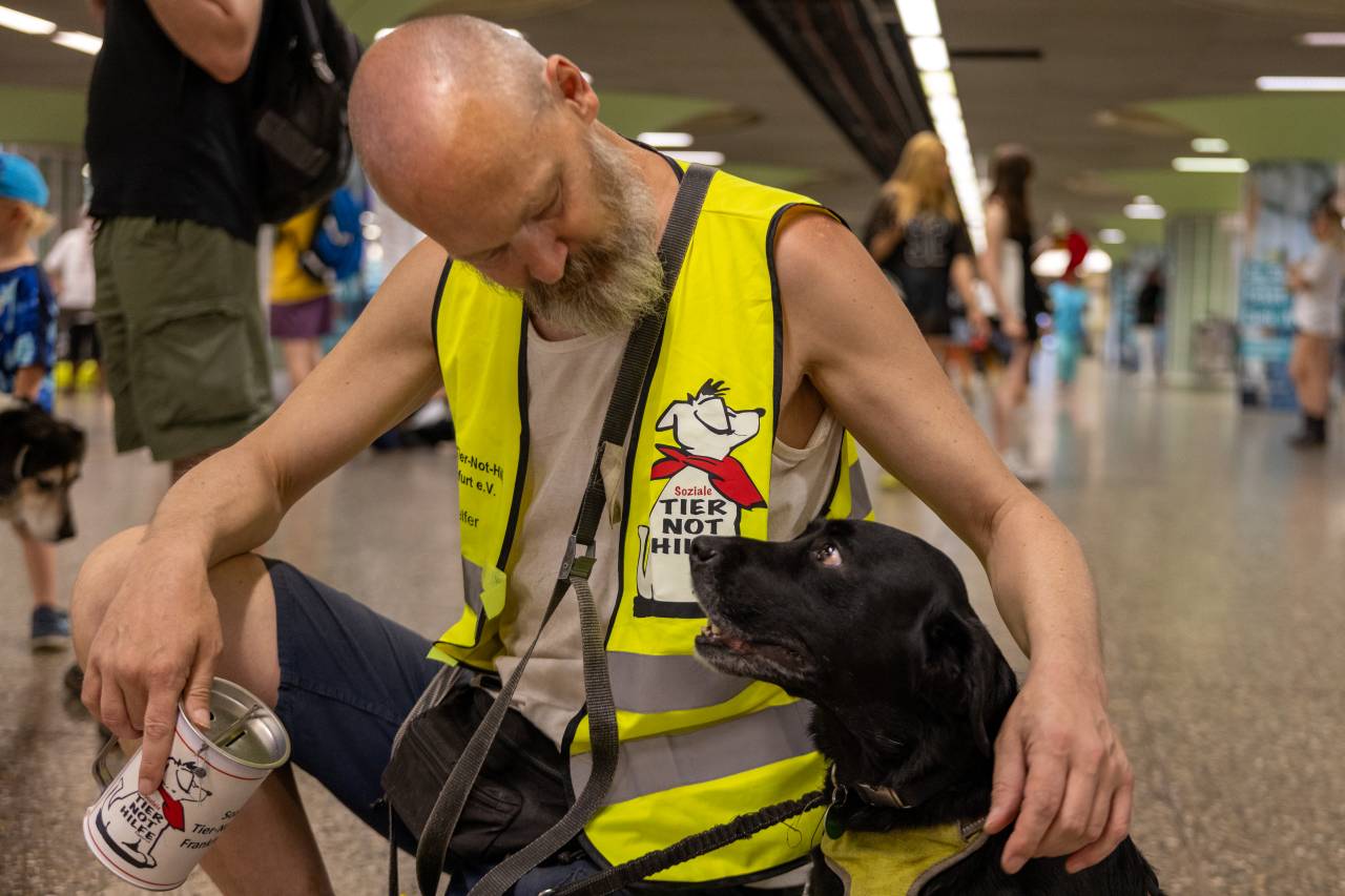 Tobi, ein dünner Mann mit Glatze und grauem Vollbart, streichelt seinen schwarzen Labrador Paul in der Hauptwache in Frankfurt
