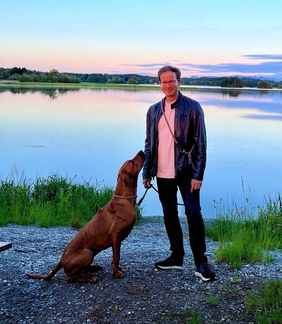 Das Bild zeigt Markus C. Müller und seinen Hund am Ufer eines Sees.