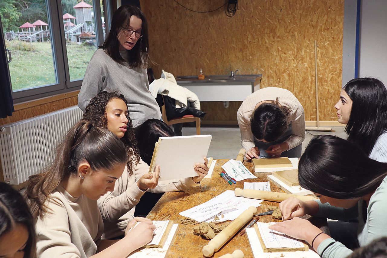 Eine Schülerinnen-Gruppe sitze an einem Tisch und fertig Tontafeln an.