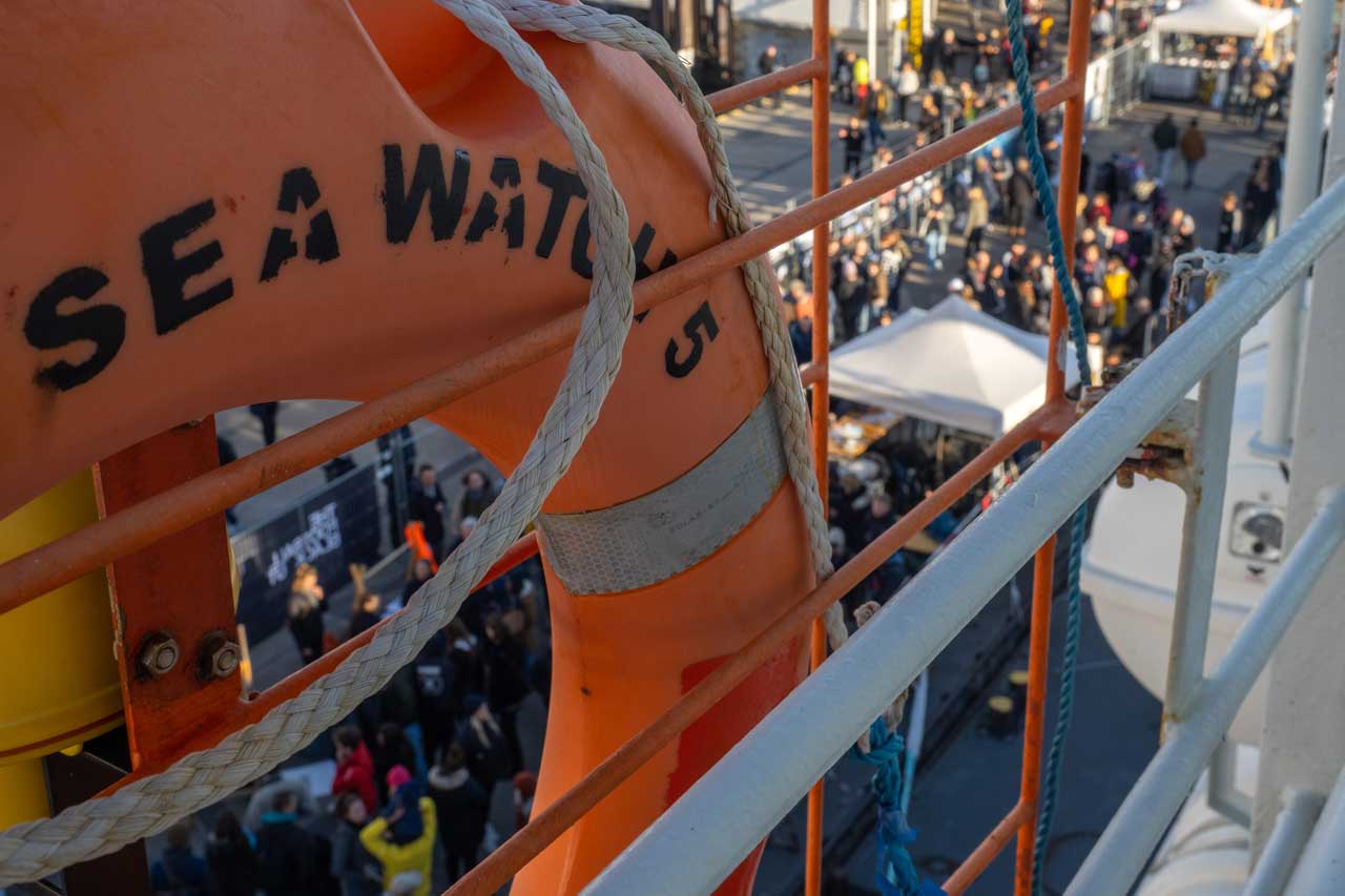 Rettungsring der Sea-Watch 5, im Hintergrund Menschen, unscharf dargestellt