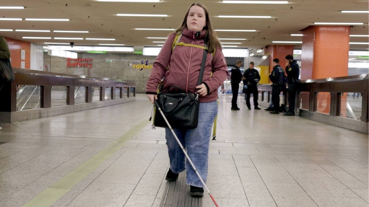 Die 23-Jährige Olivia Möller trägt eine dunkelrote Jacke und läuft mit ihrem Blindenstock durch den Stuttgarter Hauptbahnhof.