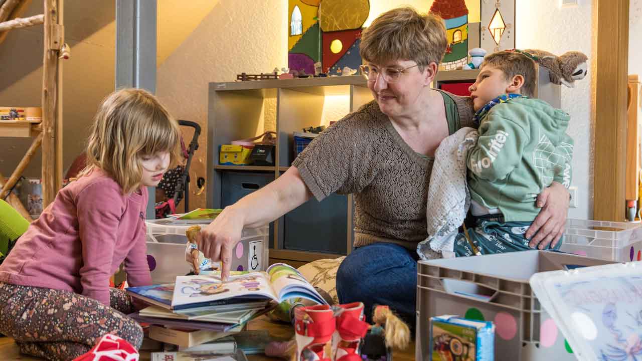 Mutter sitzt inmitten der Spielsachen mit ihren beiden Kindern