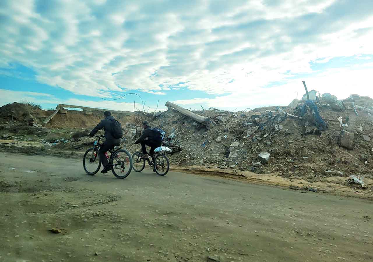 Zwei Menschen radeln im Gazastreifen vor Trümmern