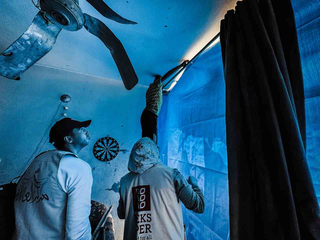 Mitarbeiterin von HEKS bringt Plane an zerstörtem haus im Gazastreifen an