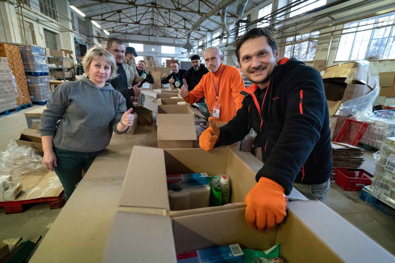 An der Packlinie stellen Mitarbeiter, die selbst ihre Heimat im Osten des Landes verlassen mussten, die Lebensmittel- und Hygieneartikel in handlichen Hilfspaketen für notbedürftige Familien und Einzelpersonen zusammen.