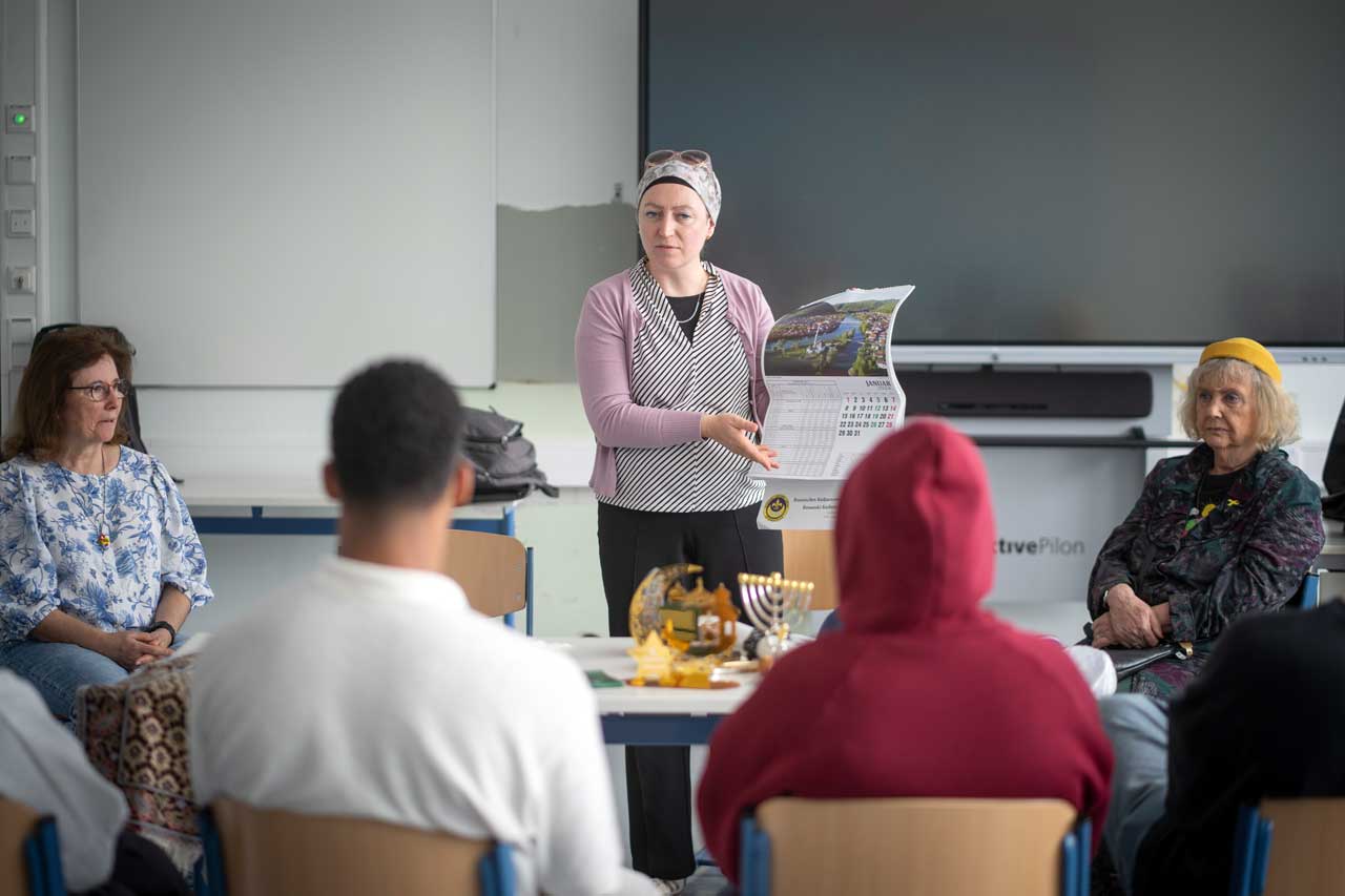 Jasmina steht vor der Klasse und hält einen Kalender. Sie erklärt die Fastenzeit Ramadan. 
