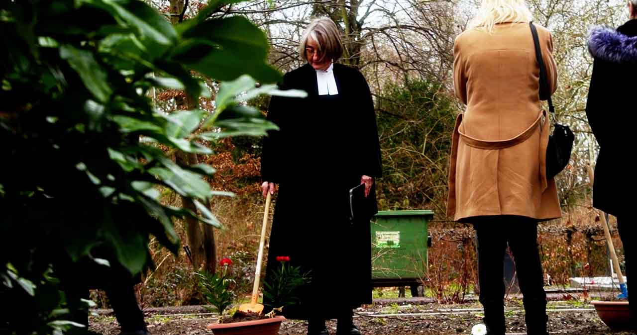 Menschen stehen mit Pfarrerin am Grab