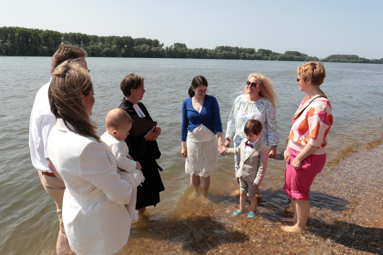 Eine Familie steht mit den Füßen im Rhein. Sie wollen ein Kind taufen lassen