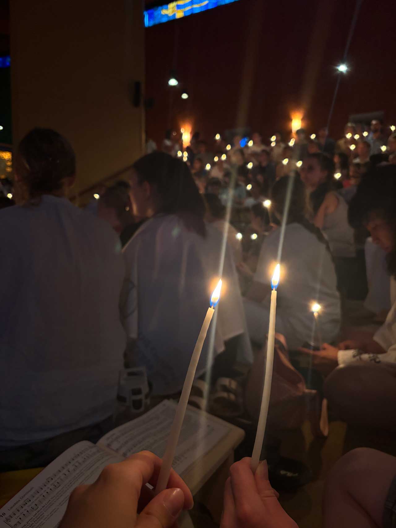 Ein Kirchraum, die Menschen halten dünne Kerzen in der Hand und vor der Fotografin liegt ein Gesangbuch. Wir sind in einer Kirche.