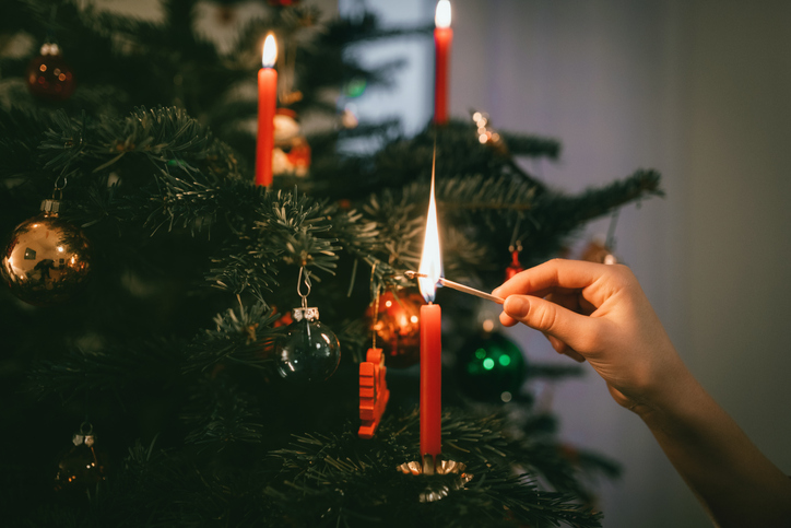 Hand zündet Kerze an Weihnachtsbaum an