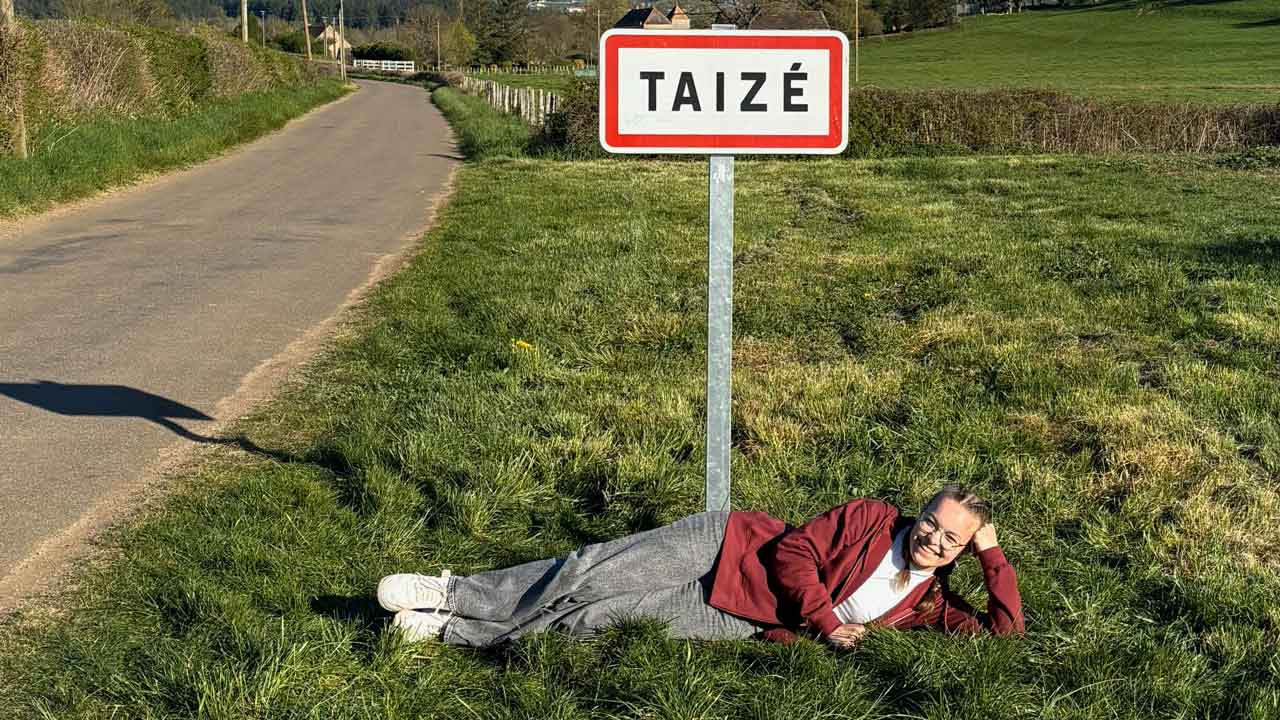 Pauline liegt auf einer Wiese vor dem Ortsschild von Taizé