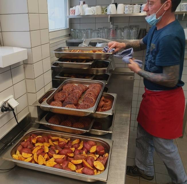 Ein Koch der ada_kantine stapelt Essensbehälter, die gefüllt sind mit Bratkartoffeln