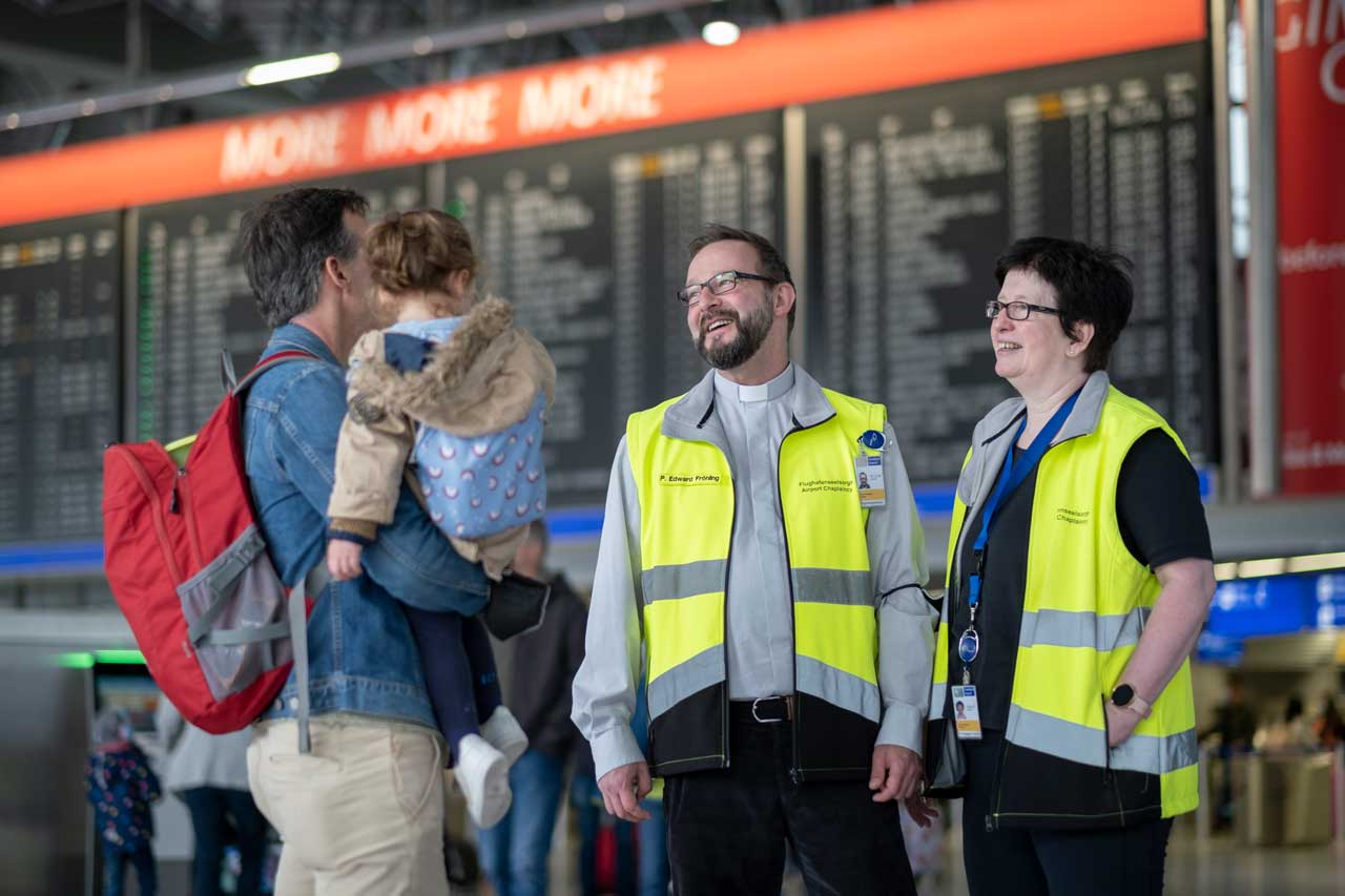 Der katholische Pater Edward Fröhling und die evangelische Pfarrerin Bettina Klünemann sprechen mit Reisenden am Flughafen Frankfurt im Terminal 1.