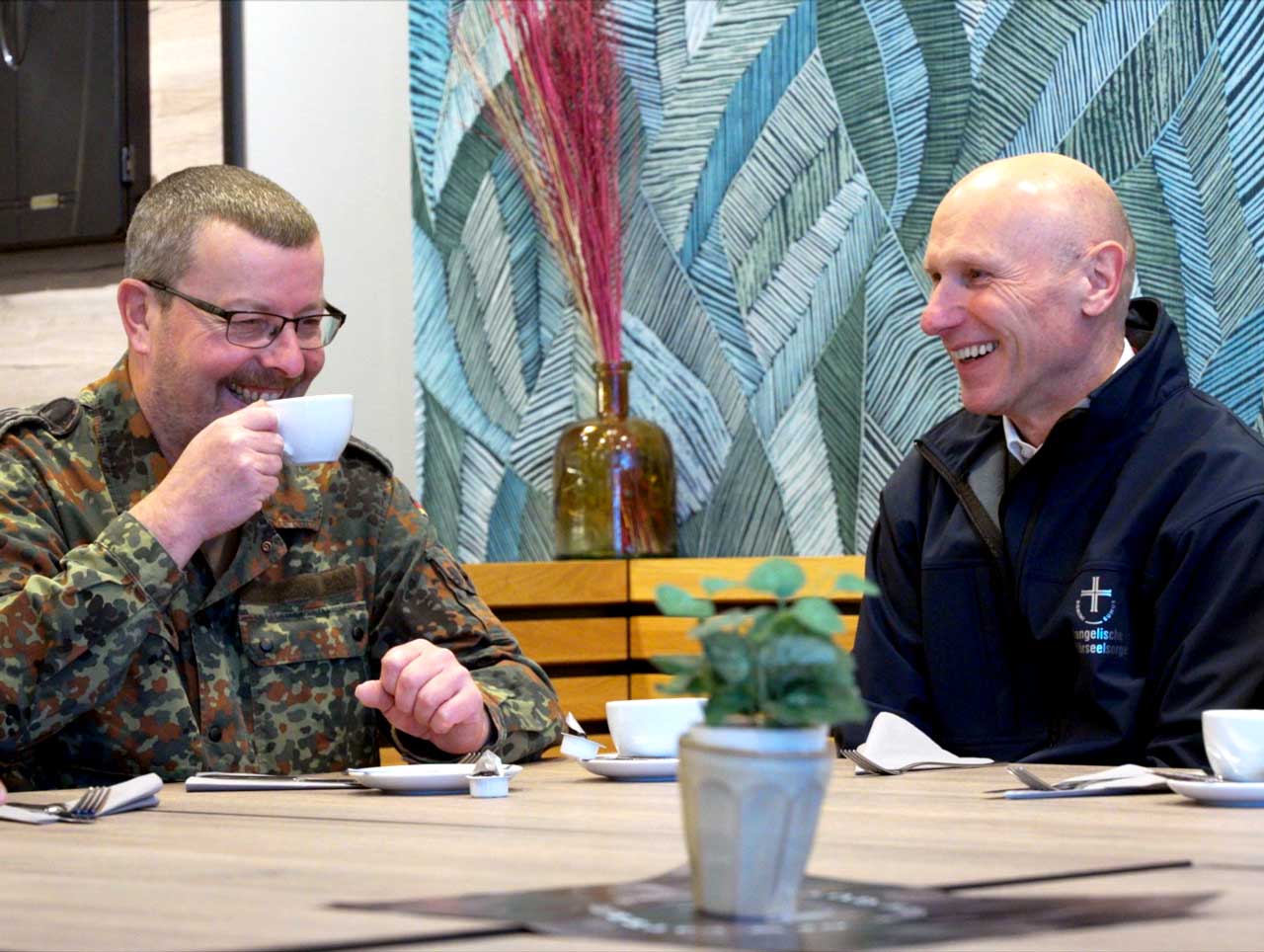 Soldat und Pfarrer sitzen im Kirchencafé nach dem Gottesdienst bei einer Tasse Kaffee zusammen