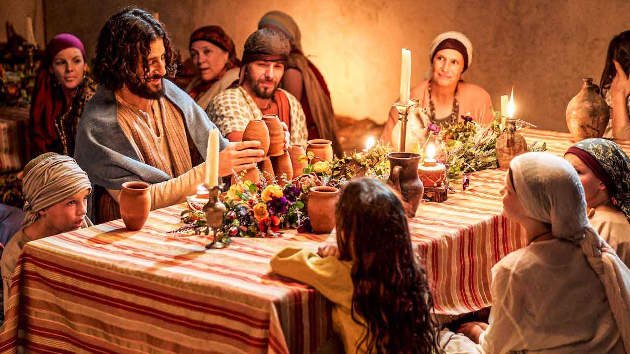 Jesus sitzt bei der Hochzeit zu Kanaa mit anderen Gästen am Tisch.