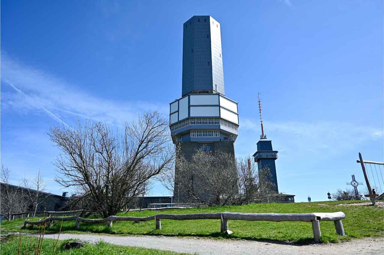 Zwei hohe Türme auf dem Gipfel des Feldbergs im Taunus. Im Vordergrund Wiese und knospende Büsche
