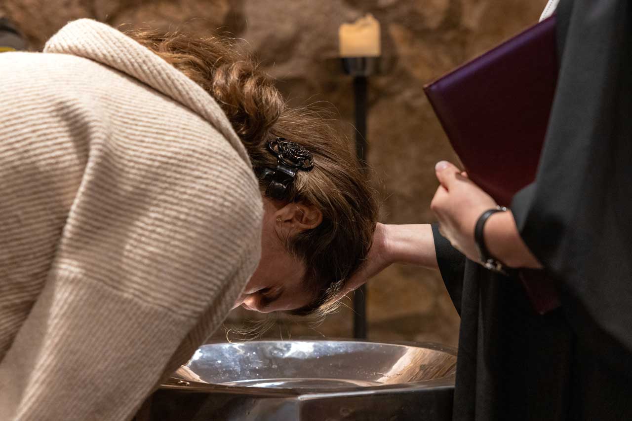 Junge Frau beugt sich über das Taufbecken und wird gerade getauft.