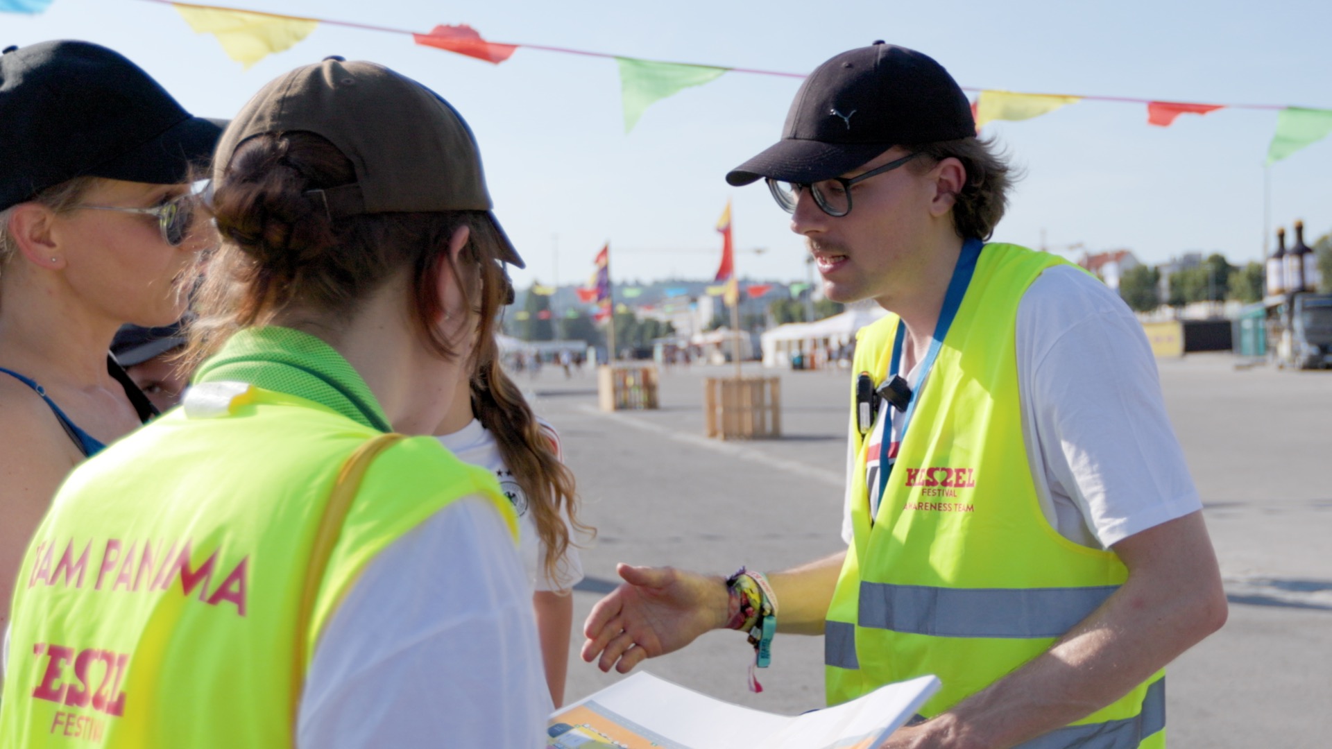 Zwei Personen in gelben Warnwesten mit der Aufschrift Panama sprechen mit Besucherinnen auf dem Festivalgelände