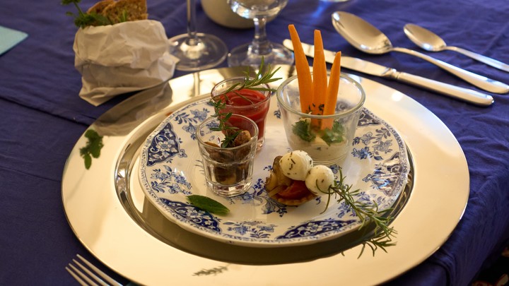 Ein edler Teller aus blau-weißem Zierporzellan. Darauf liegen verschiedene Köstlichkeiten, ansprechend angerichtet. Zu sehen sind verschiedene Dipps, Tomate-Mozzarella, Karotten-Sticks, Rosmarinzweige und eine kleine Portion frisches Brot.